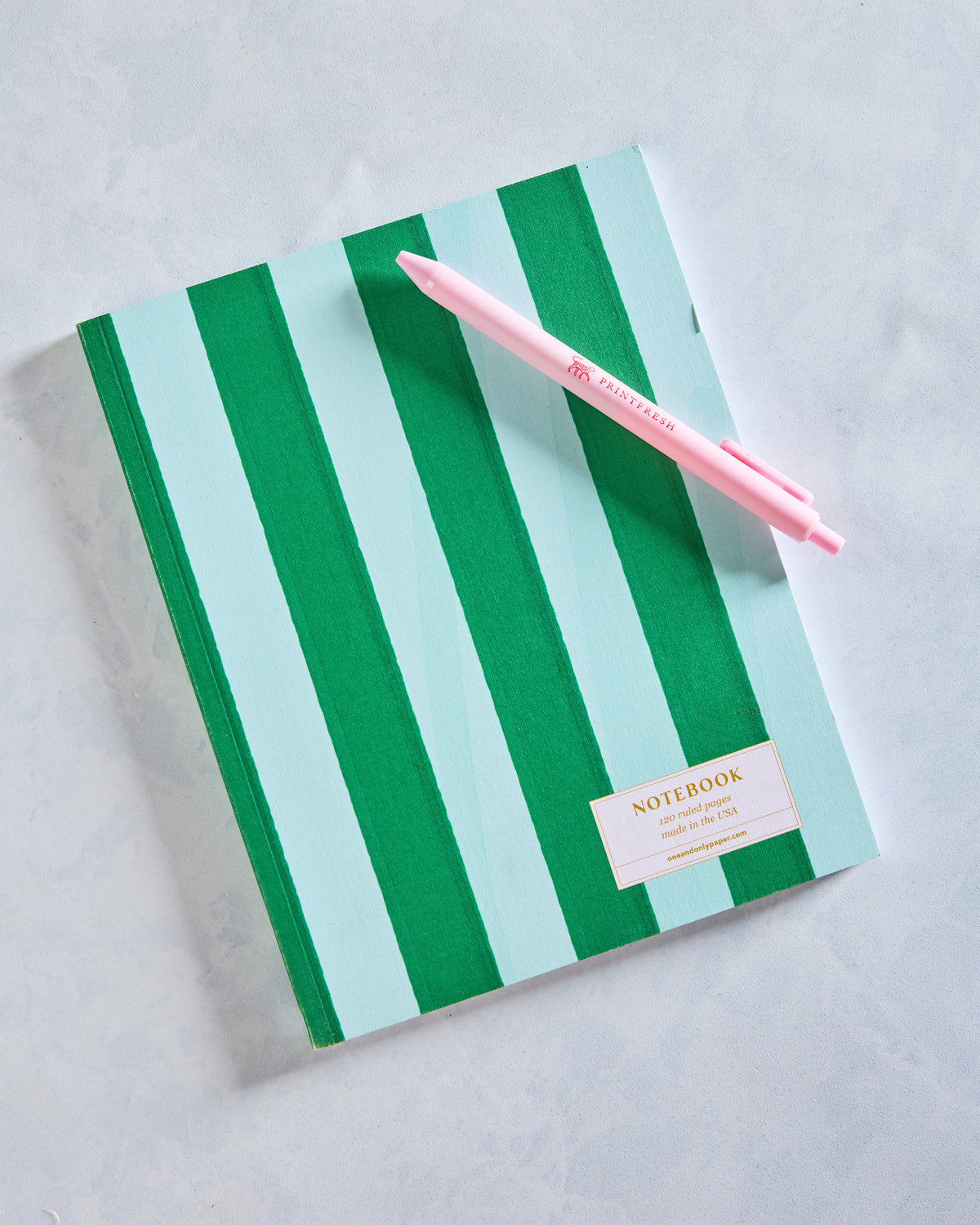 Closed journal with alternating green and pale aqua vertical stripes, shown with a pink pen.
