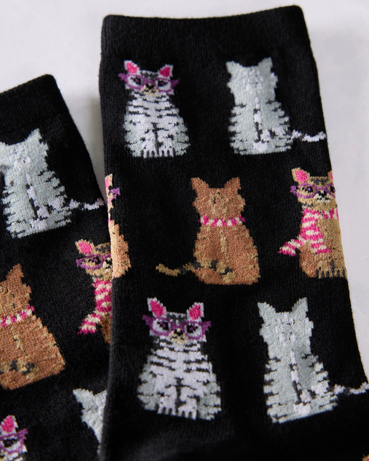 Close-up of black crew socks patterned with repeated gray and brown cats, including cats wearing glasses and striped scarves.