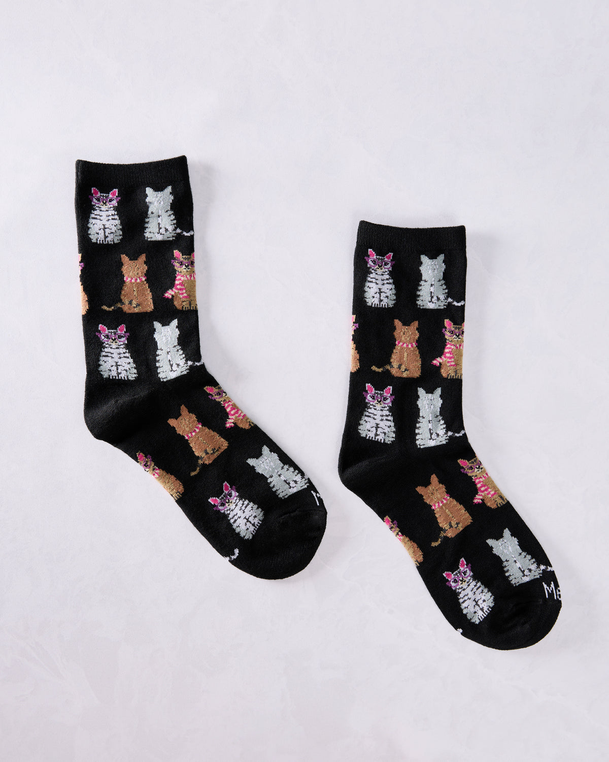 Pair of black crew socks displayed separately with repeated gray and brown cats, including cats wearing glasses and striped scarves.