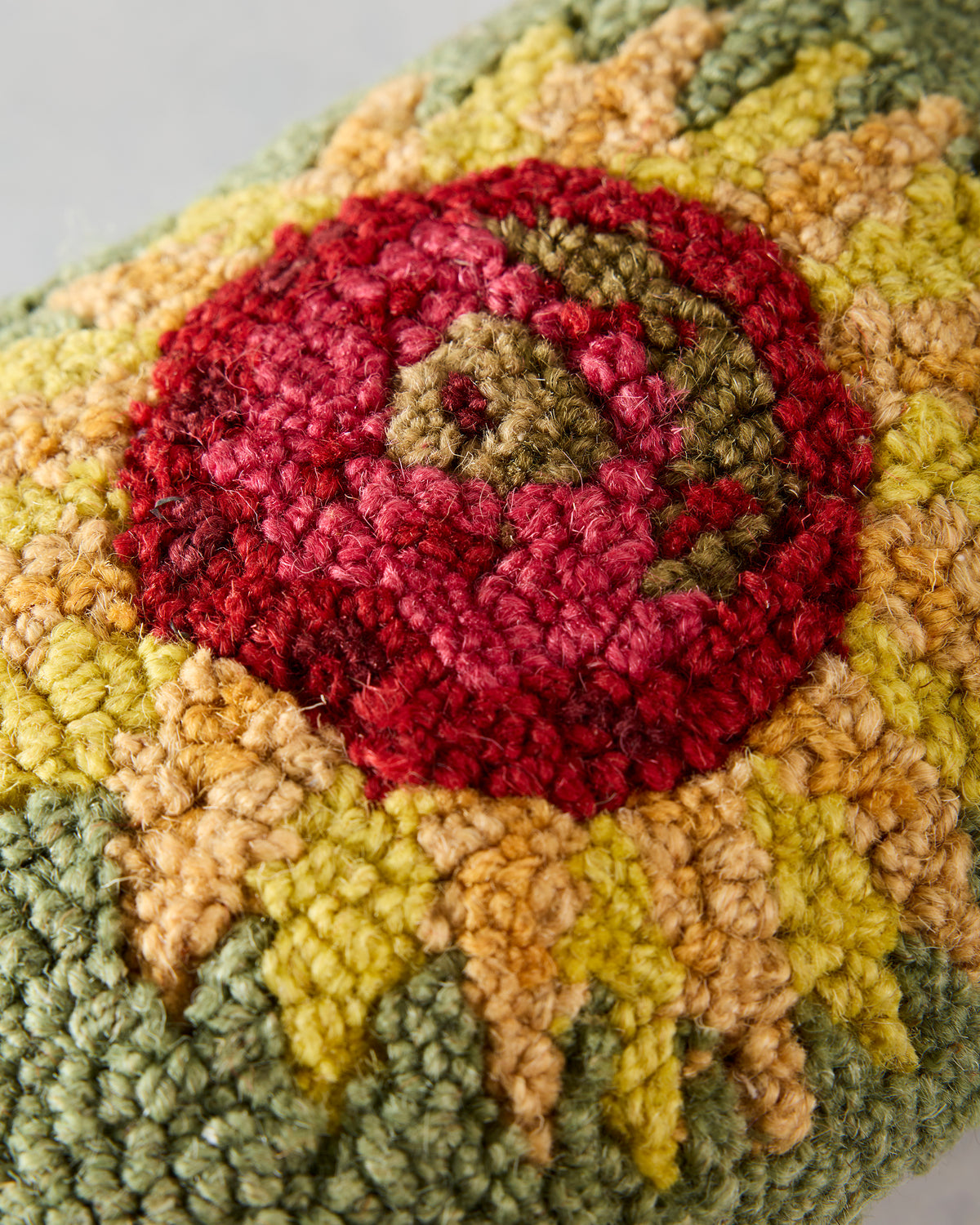 Close-up of a green sunflower pillow with a red, yellow, and tan hooked floral design.