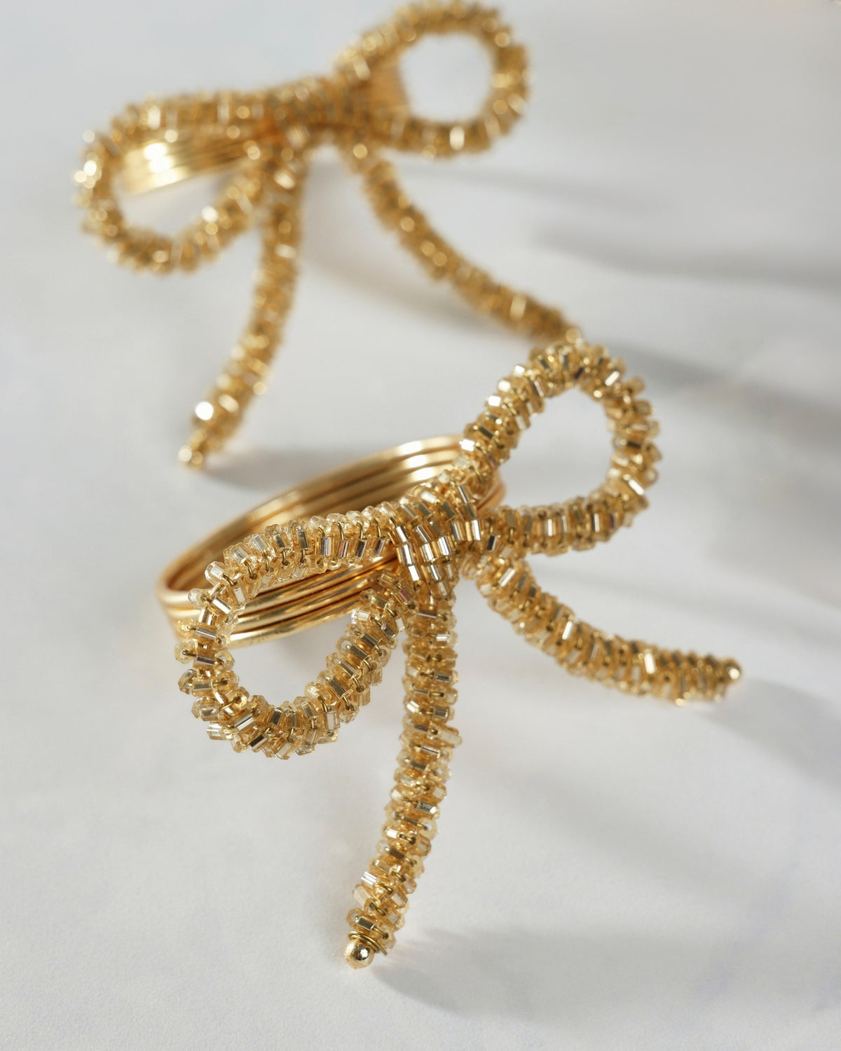 Close-up of two gold bow napkin rings with beaded detailing and trailing bow tails.