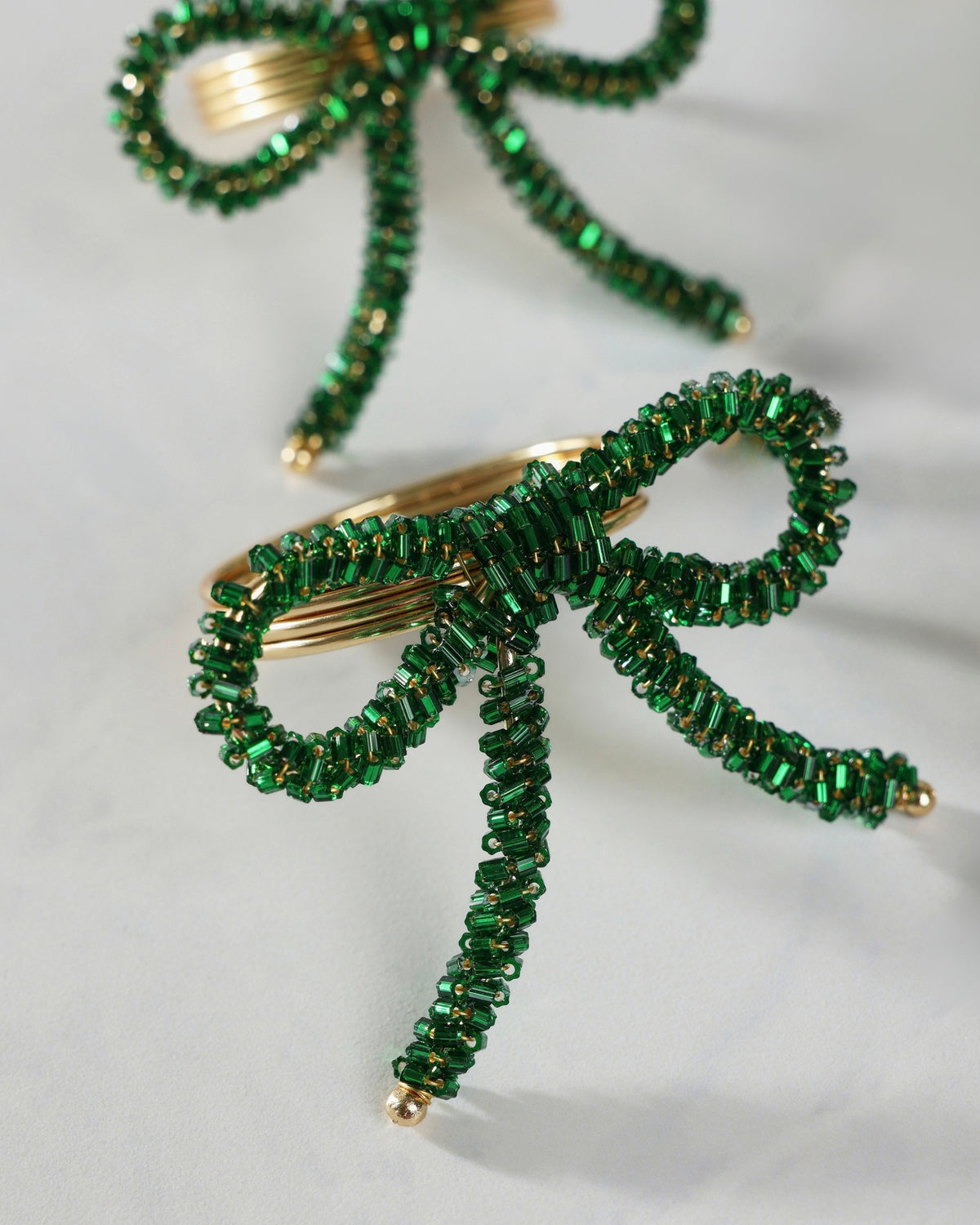 Green beaded bow napkin ring with a gold-tone metal center and dangling beaded tails