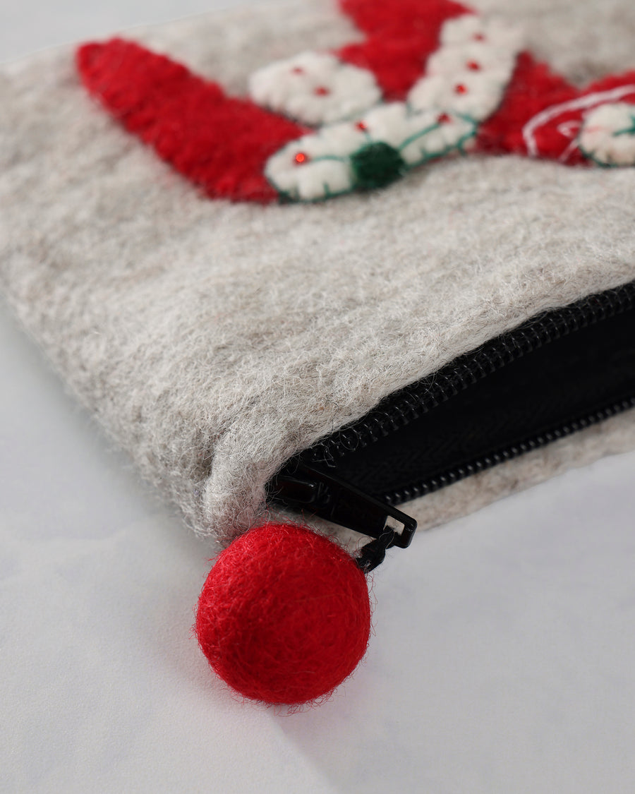 Close-up of an ivory dala horse purse with a black zipper and red pom-pom