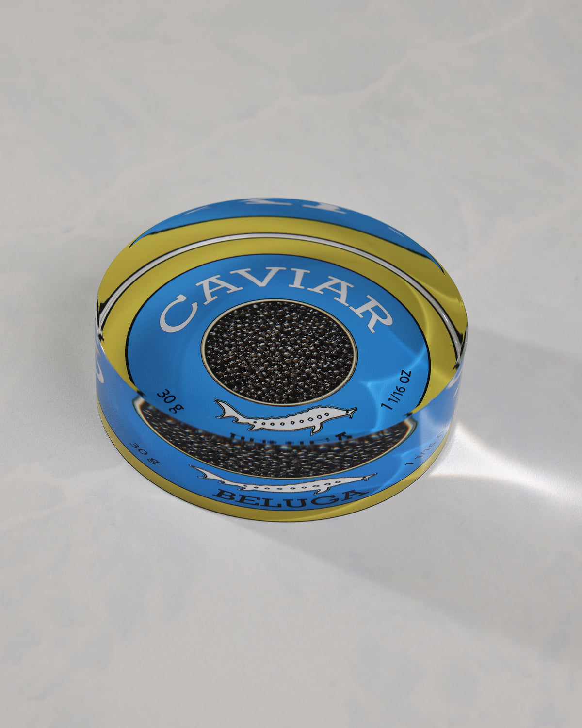 Angled view of a round blue-and-gold caviar-themed napkin weight showing its raised profile and Beluga label.