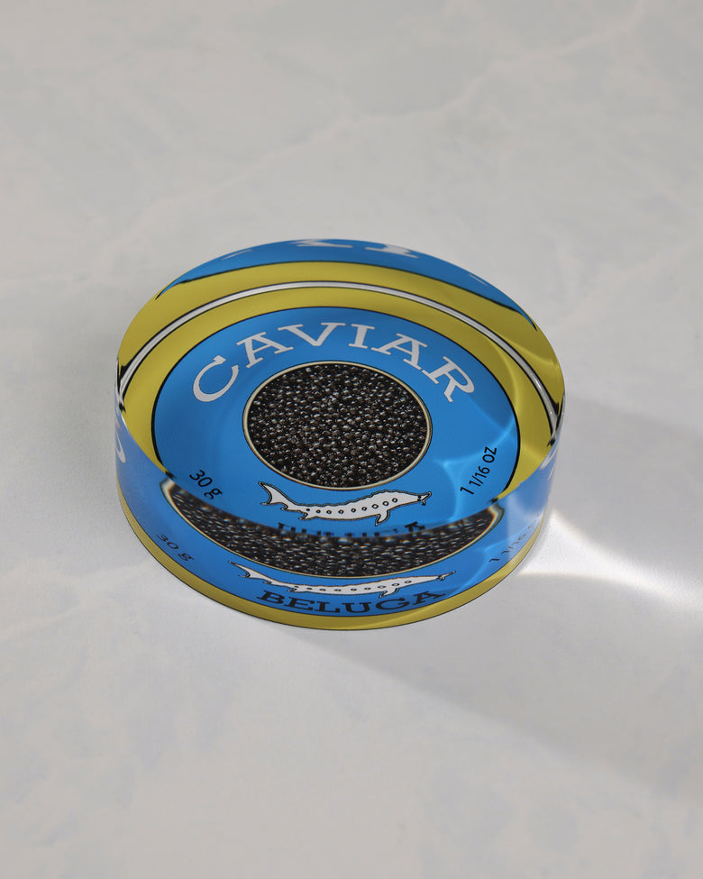 Angled view of a round blue-and-gold caviar-themed napkin weight showing its raised profile and Beluga label.