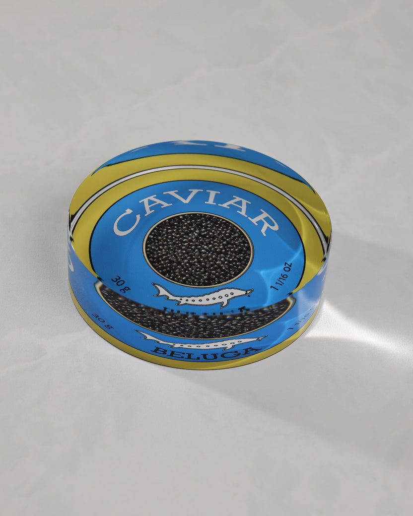 Angled view of a round blue-and-gold caviar-themed napkin weight showing its raised profile and Beluga label.
