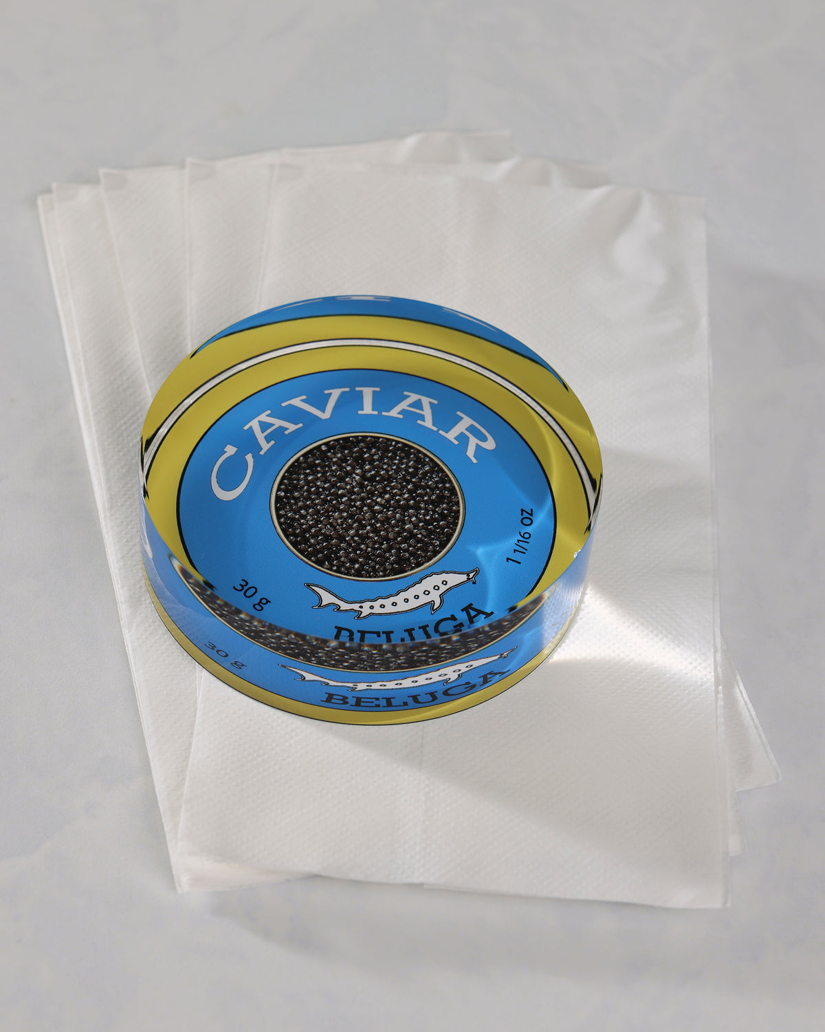 Round blue-and-gold caviar-themed napkin weight resting on folded white napkins.
