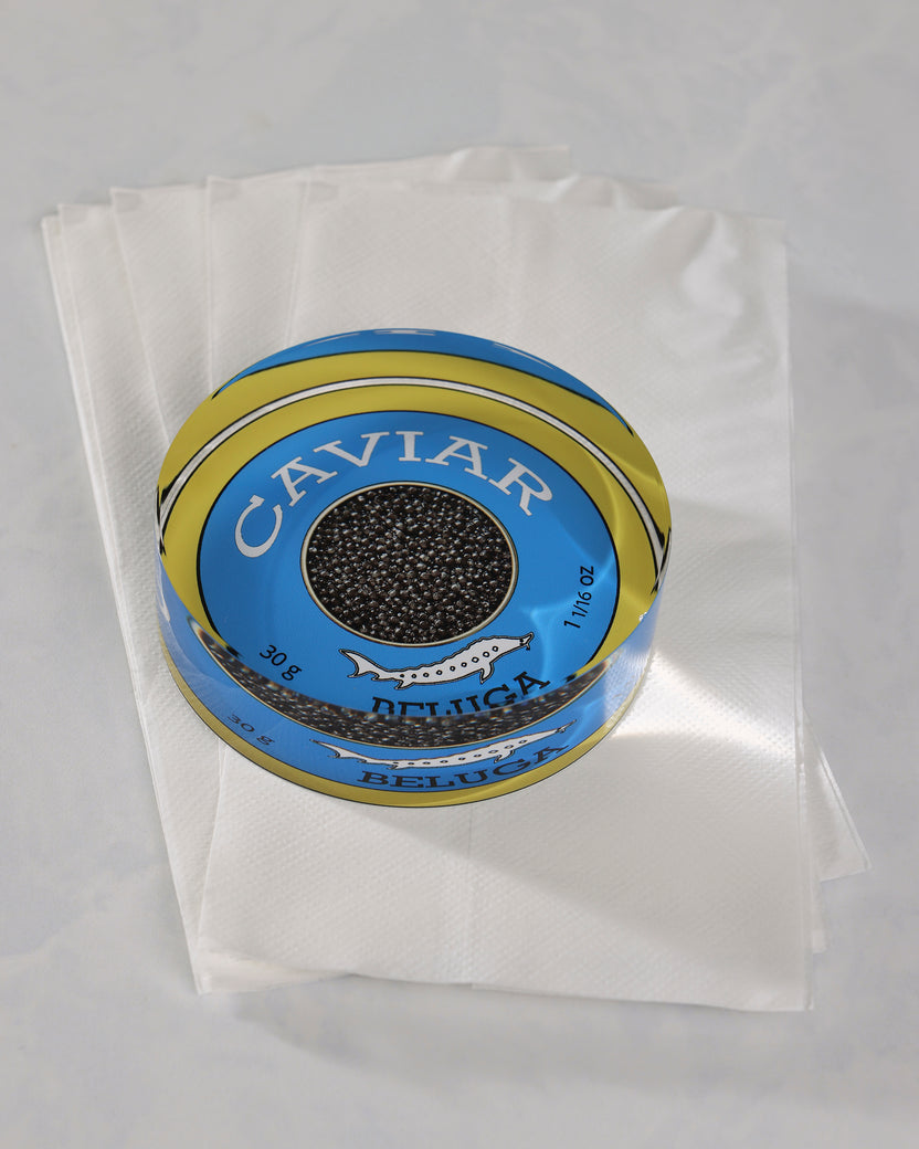 Round blue-and-gold caviar-themed napkin weight resting on folded white napkins.