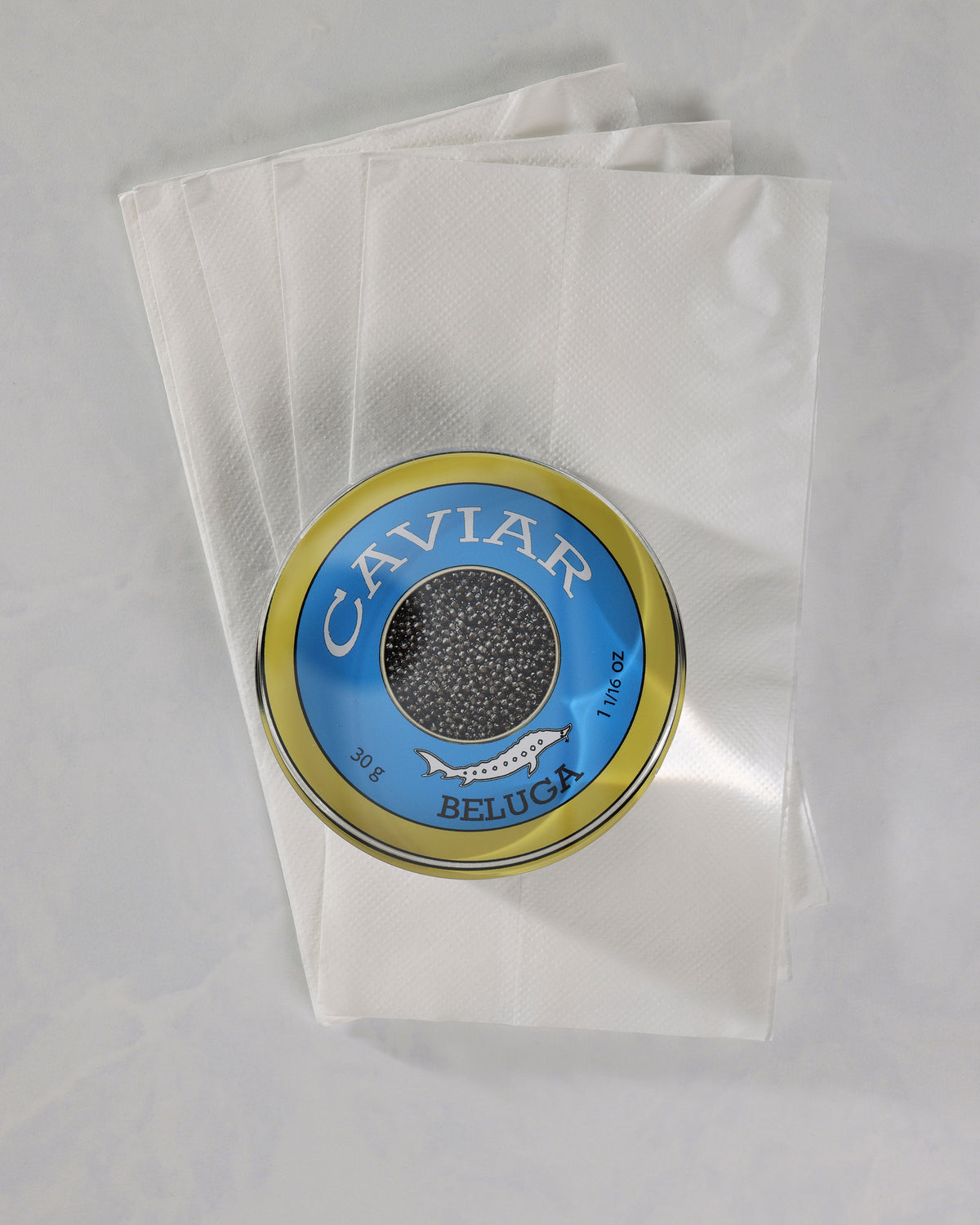 Top view of a round blue-and-gold caviar-themed napkin weight placed on several white napkins.