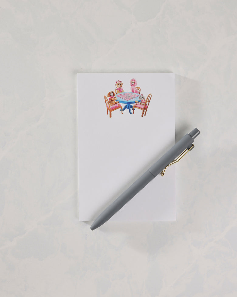 White top-bound notepad with an illustration of dogs seated around a blue table, shown with a gray pen.
