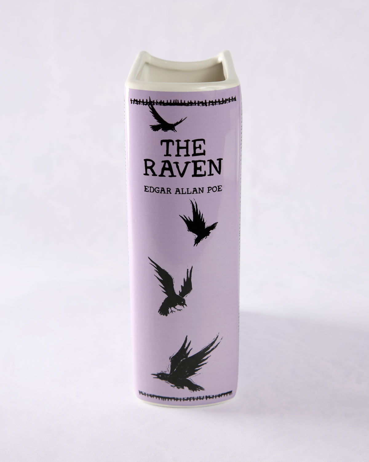 Front view of a purple ceramic book vase with black raven artwork and the title “The Raven” by Edgar Allan Poe.