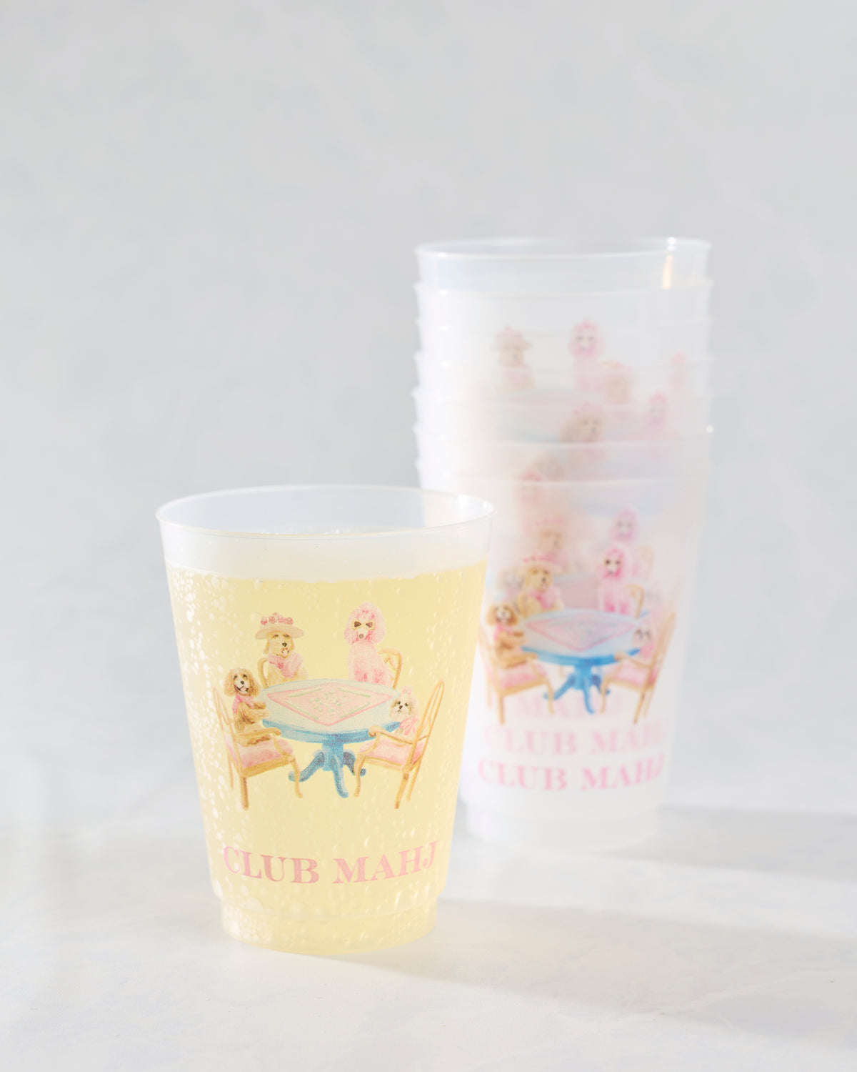 Yellow drink-filled frosted cup in front of a second white cup, both printed with dogs around a mahjong table.