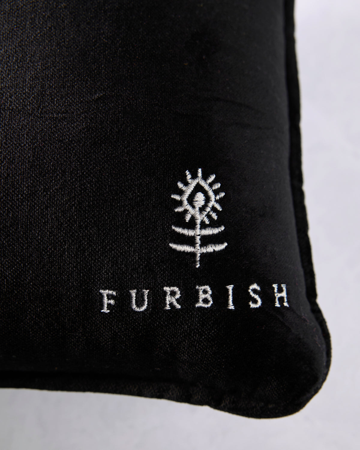 Close-up of the black pillow corner showing the embroidered Furbish logo and emblem.