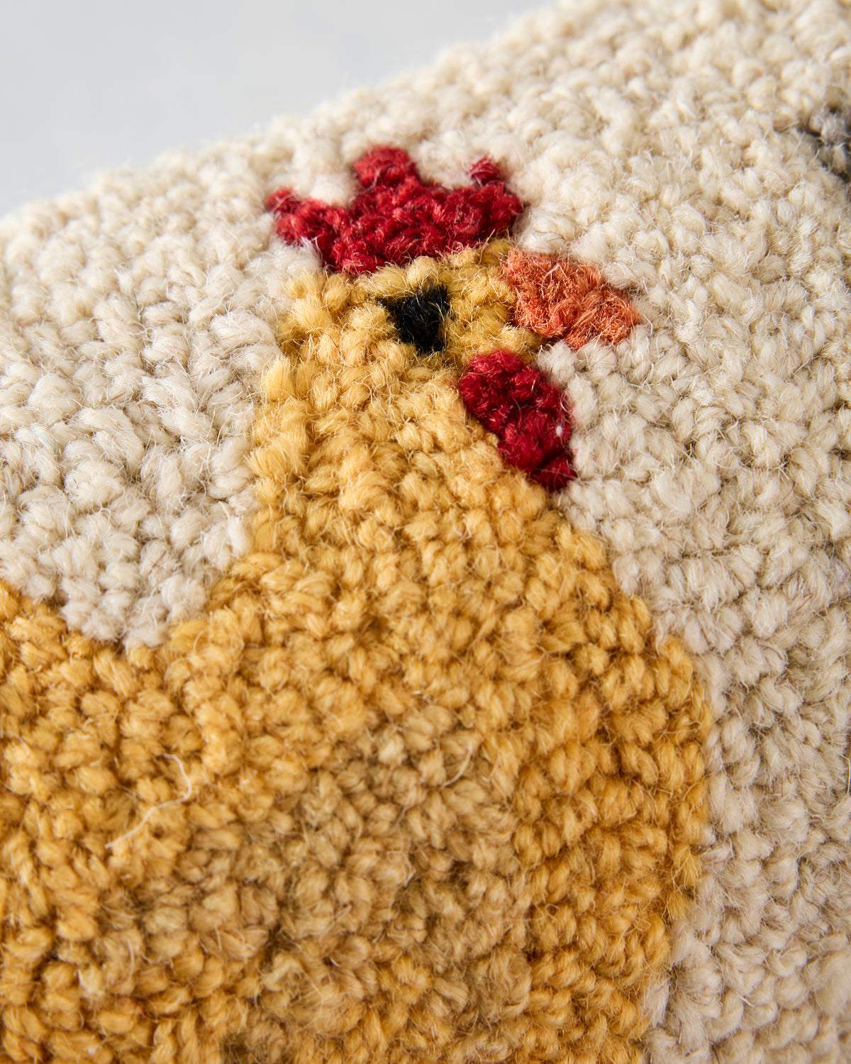 Close-up of the pillow’s hooked yellow chicken artwork, showing textured stitching and red details.