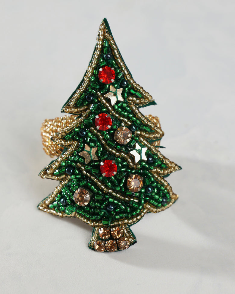Close-up of a green Christmas tree napkin ring decorated with gold beadwork, red and gold ornaments, stars, and a jeweled trunk.