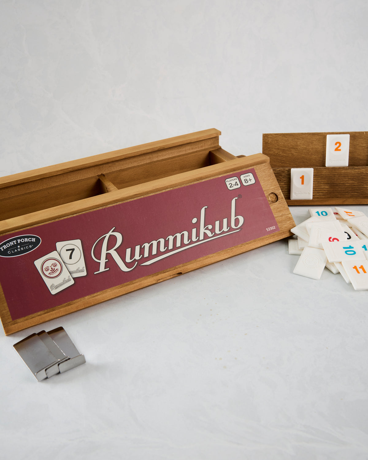 Open wooden Rummikub vintage game box with tile racks, scattered tiles, and metal hinges.