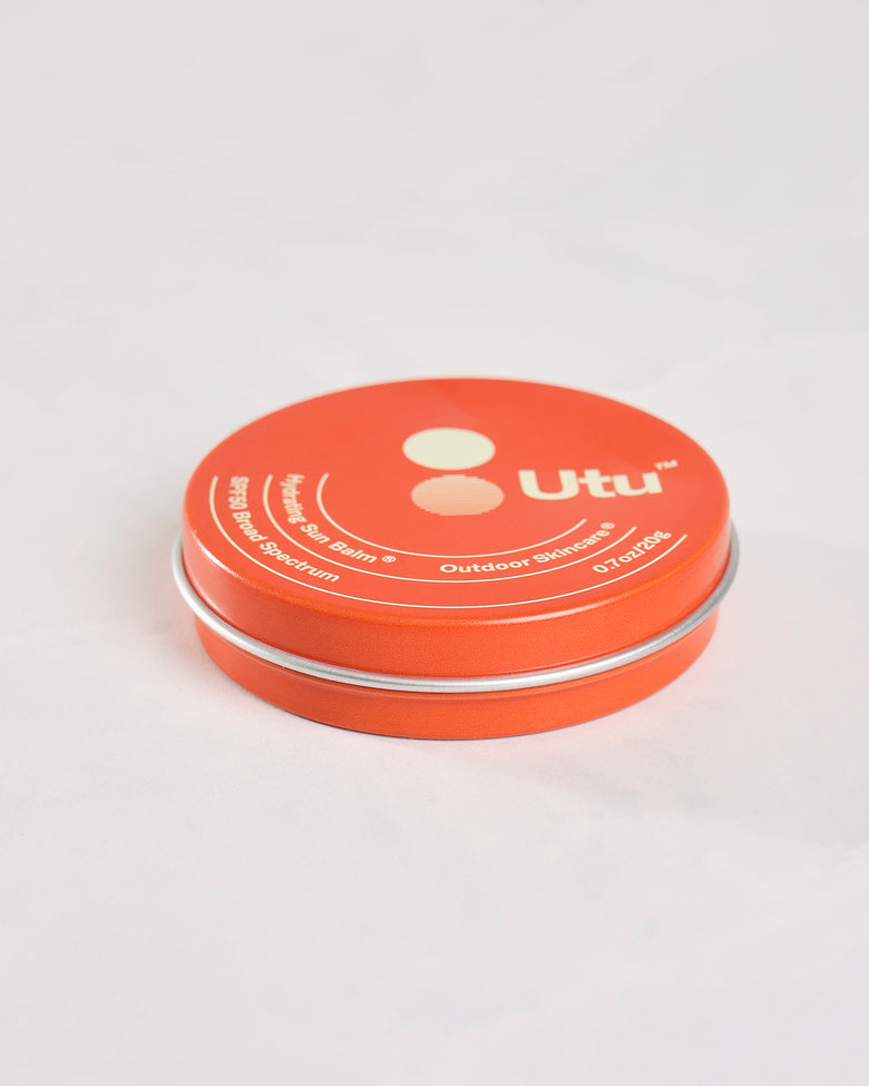 Closed orange Utu SPF50 Hydrating Sun Balm tin shown at a low angle.