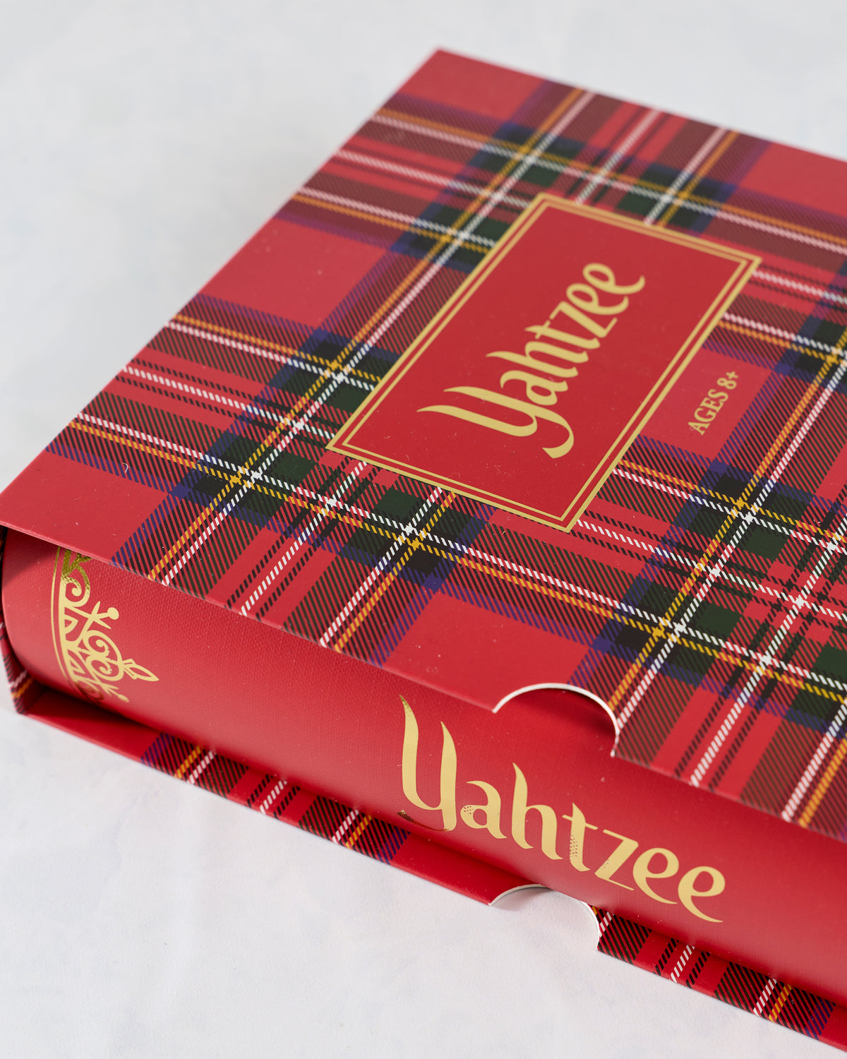 Angled close-up of the red plaid Yahtzee game case showing its gold Yahtzee lettering and red spine.