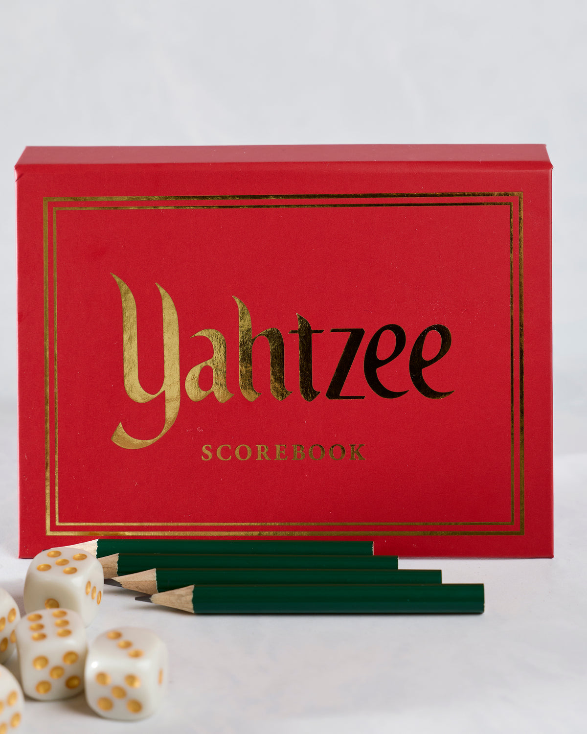 Red Yahtzee scorebook cover displayed behind green pencils and white dice.
