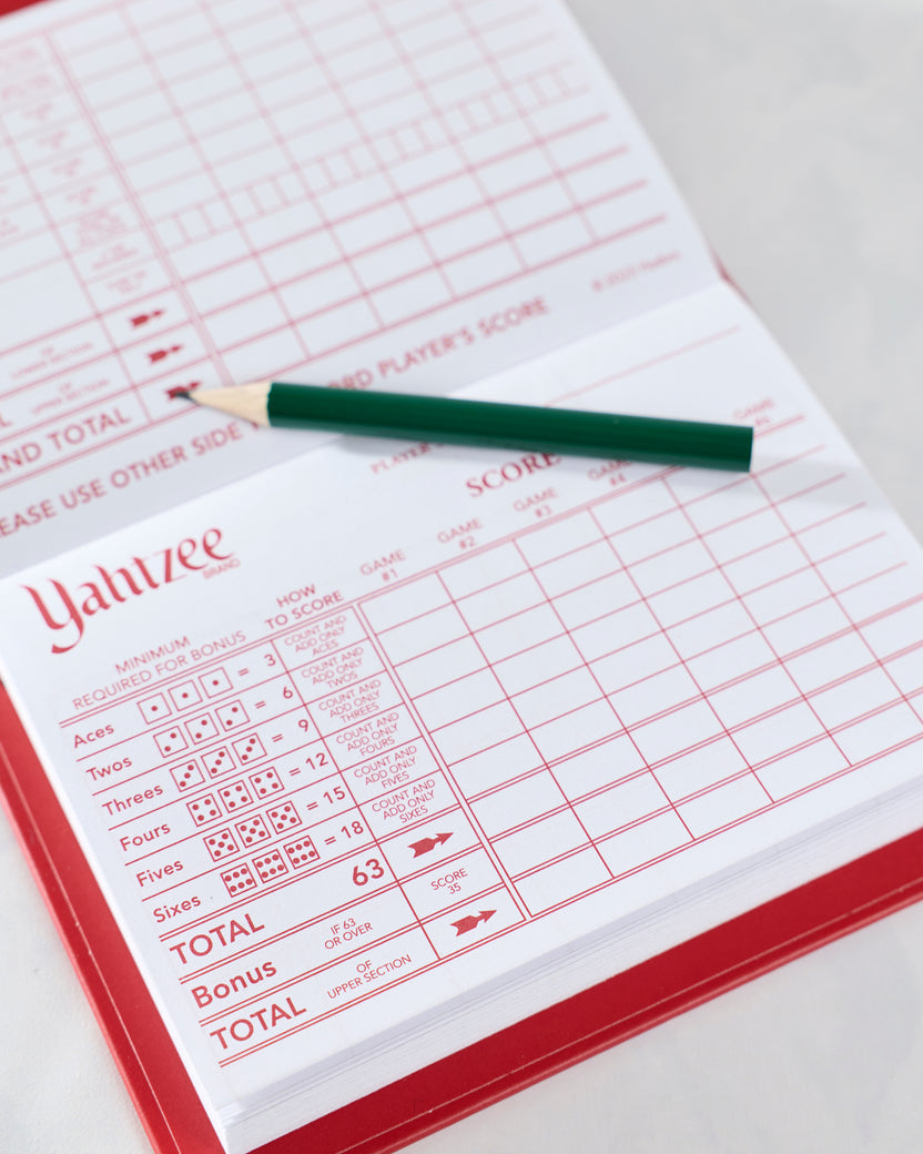 Open Yahtzee scorebook showing a scoring grid and dice-score instructions with a green pencil across the page.