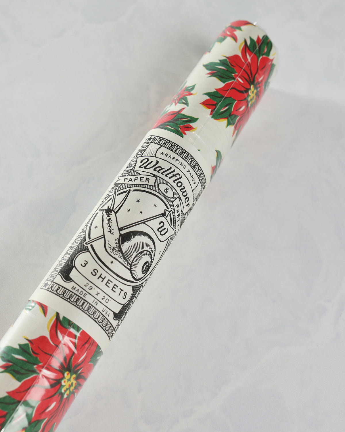 Roll of poinsettia wrapping paper with a printed Wallflower Paper label showing three sheets, 29 × 20, made in USA.