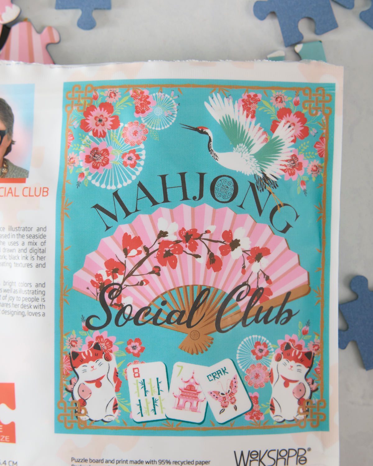Close view of the Mahjong Social Club puzzle artwork showing a crane, flowers, a pink fan, mahjong tiles, and two beckoning cats.