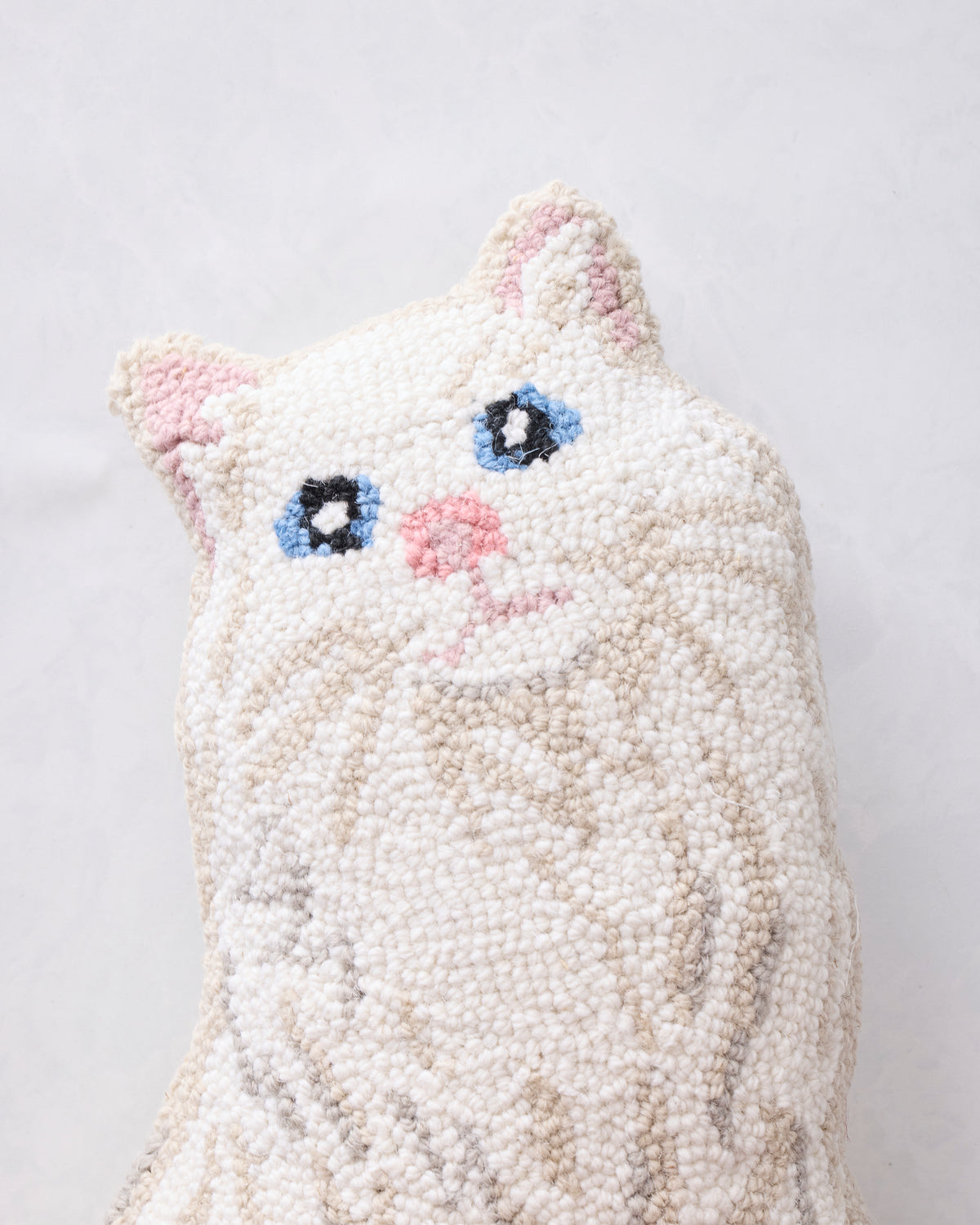 Close-up of the white cat-shaped hook pillow front with pink ears and nose, blue eyes, and stitched whiskers