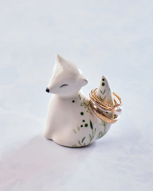 White ceramic fox ring holder shown from the front with rings arranged around its tail.