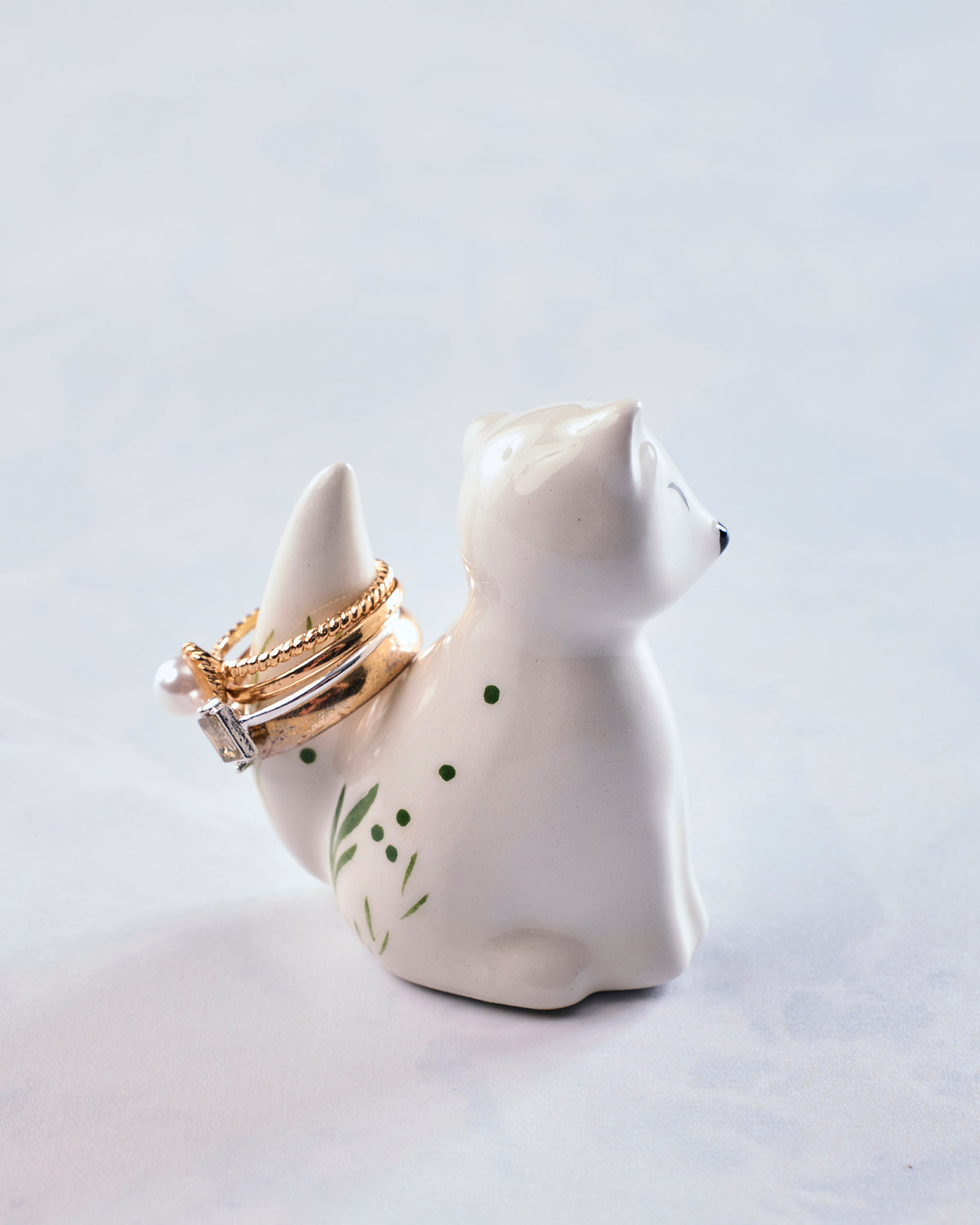 White ceramic fox ring holder shown from the back with rings arranged around its tail.