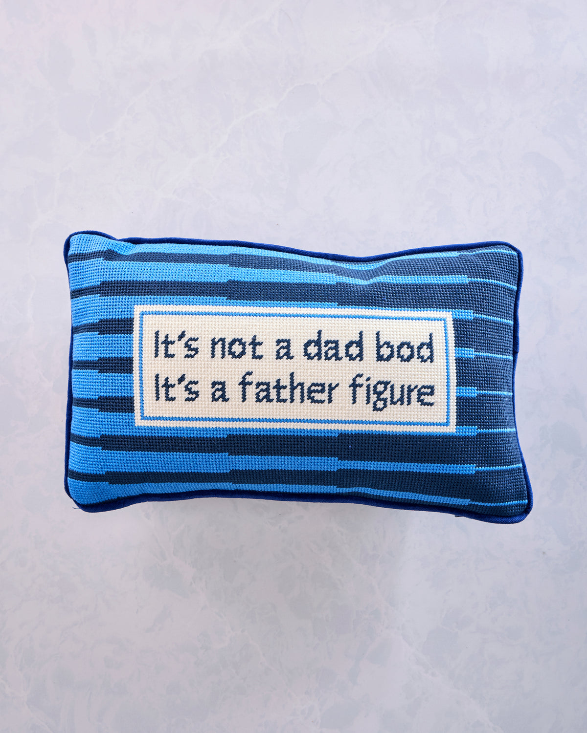 Front view of a blue and navy striped needlepoint pillow with the message “It’s not a dad bod; it’s a father figure.”