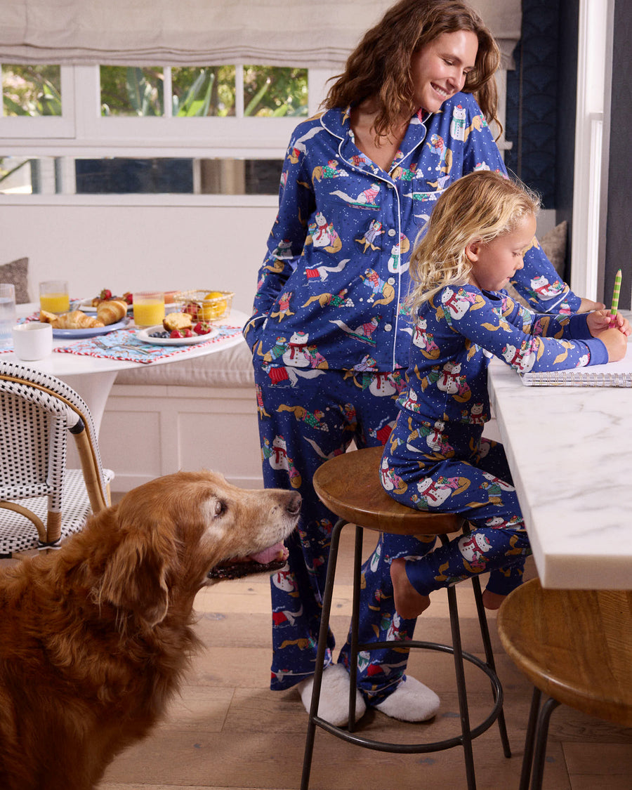 Adult and child wearing matching blue printed pajamas in a kitchen while a dog stands nearby.
