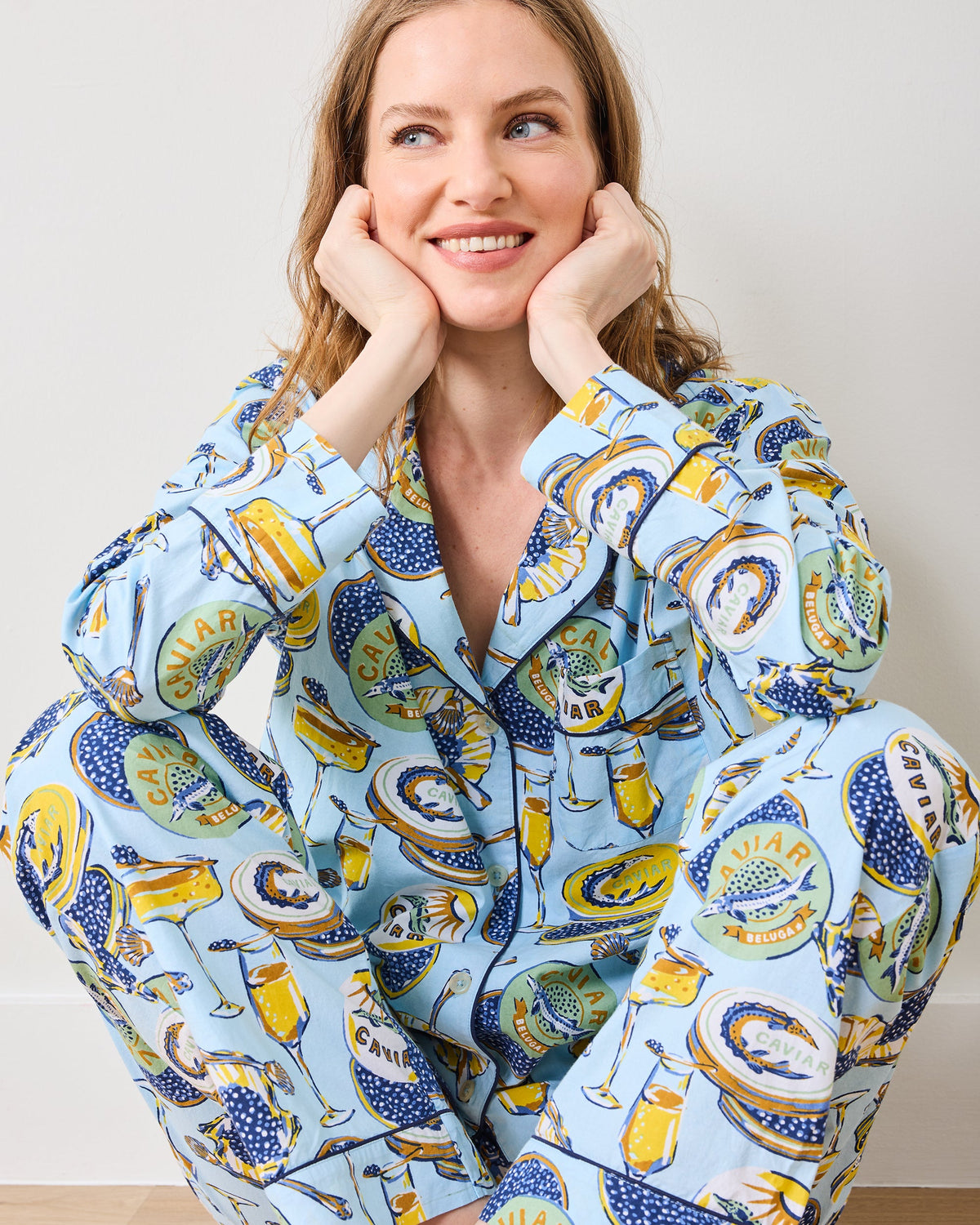 Close front view of a person wearing the pale blue Champagne & Caviar petite long pajama set, showing the notched collar, buttons, and patterned sleeves and pants.