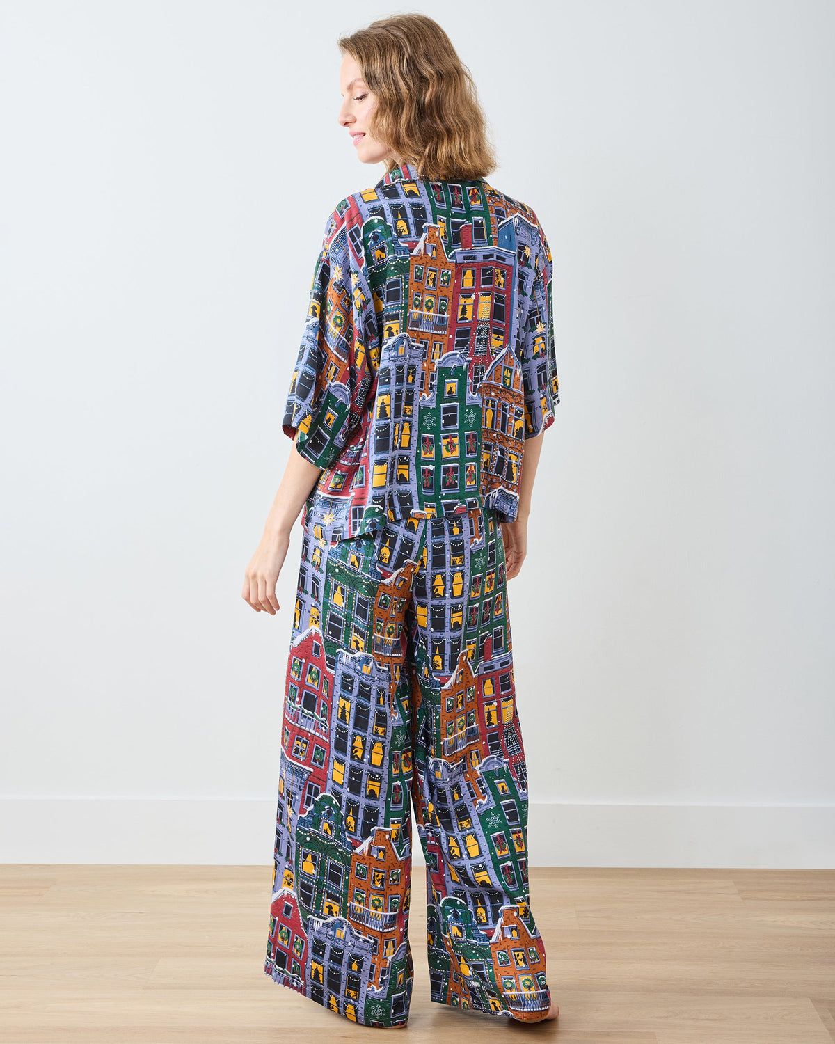Full back view of a person wearing a matching short-sleeve pajama top and wide-leg pants with a colorful city-building print.