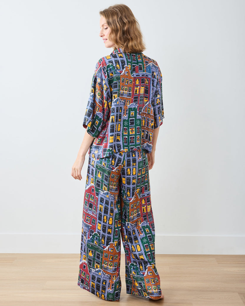 Full back view of a person wearing a matching short-sleeve pajama top and wide-leg pants with a colorful city-building print.