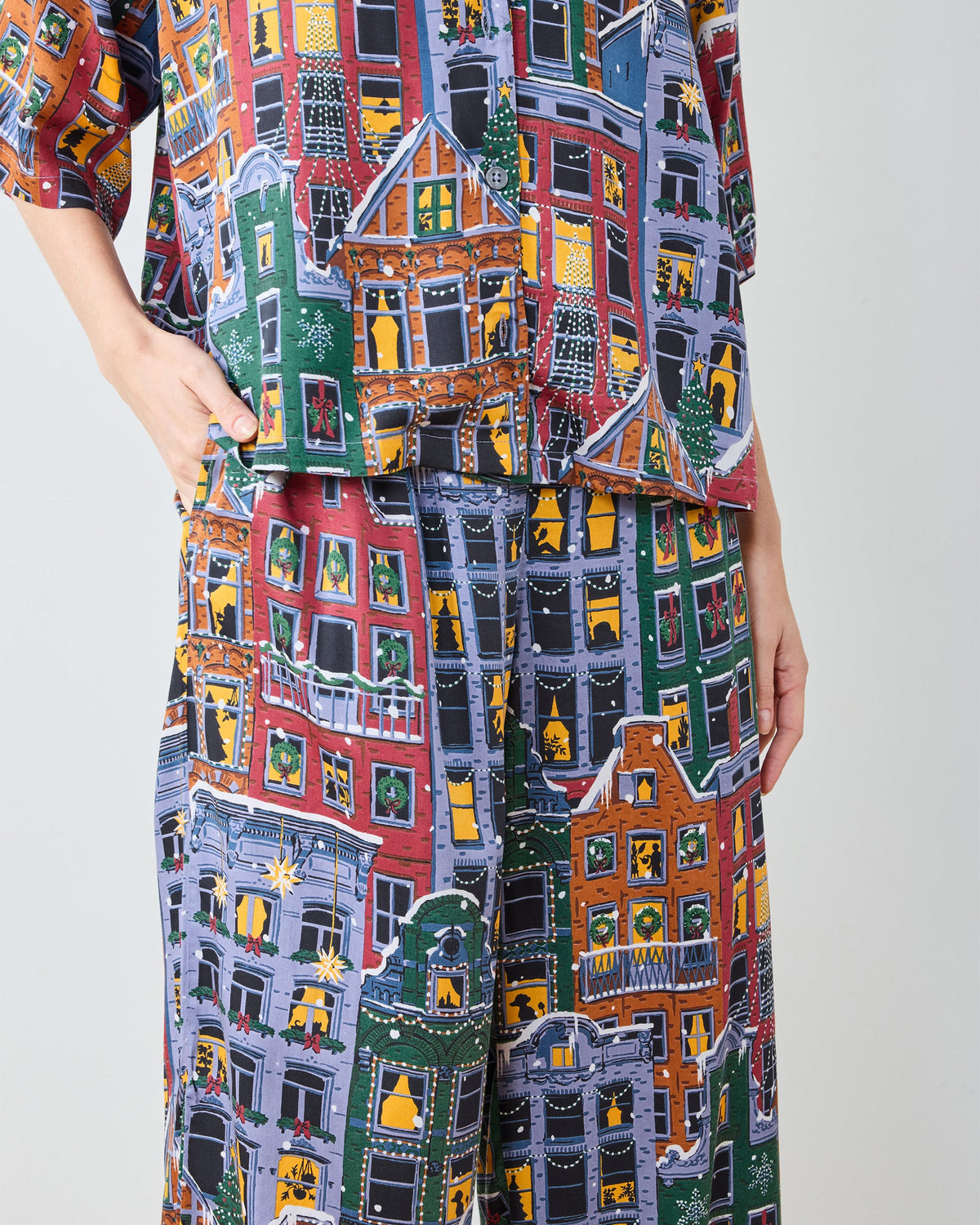 Close-up of the patterned pajama top hem and pants, showing illustrated city buildings, windows, wreaths, and holiday trees.