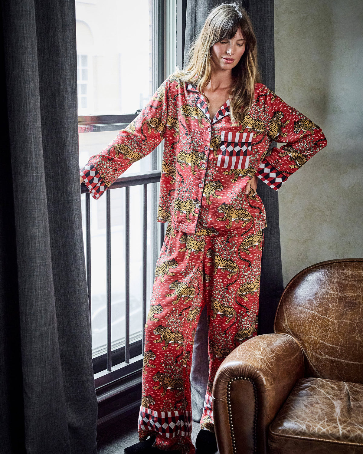 Model standing beside a window wearing a red leopard-print pajama shirt and wide-leg pants with checkerboard trim.