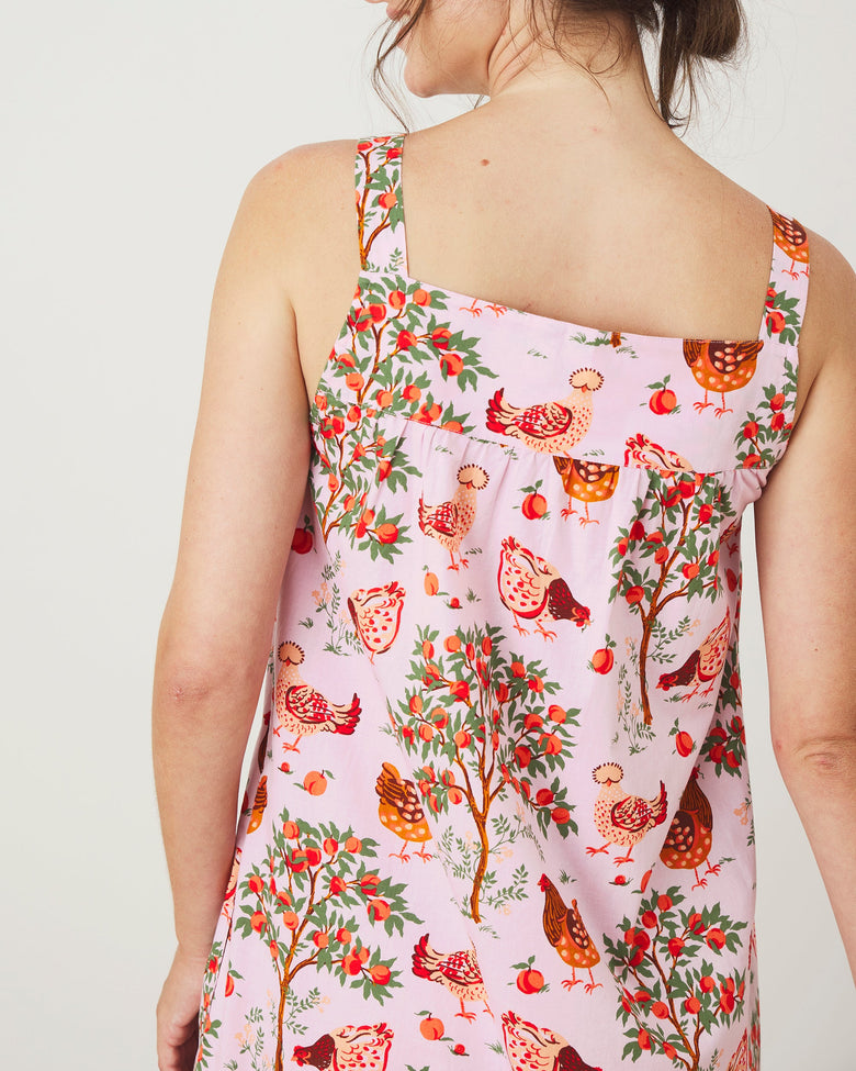 Back view of a ballet-pink sleeveless nightgown with shoulder straps, a straight upper back panel, and a hen, fruit, and leafy-tree print.
