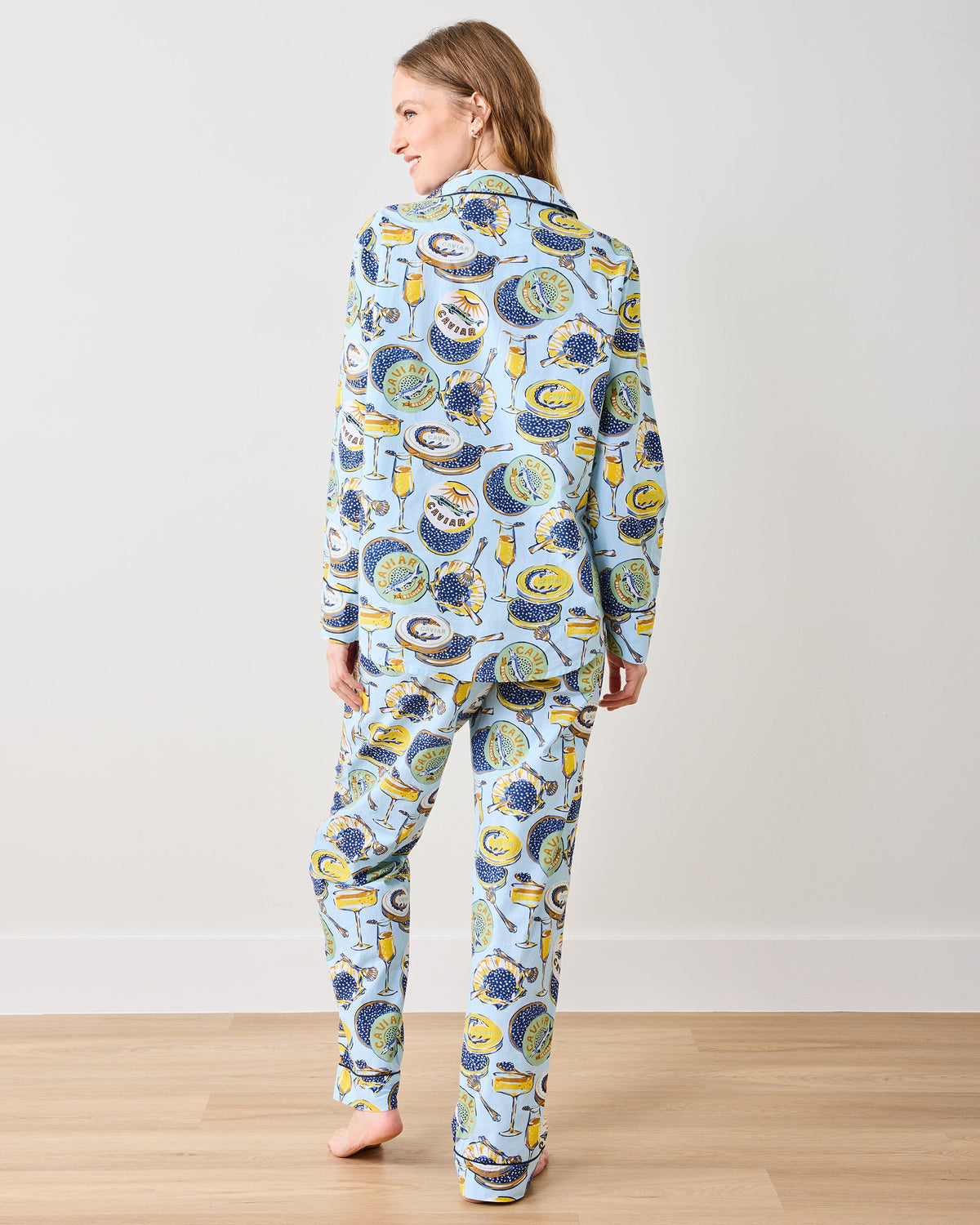 Back view of a person wearing the pale blue Champagne & Caviar petite long pajama set with a patterned button-front top and matching pants.