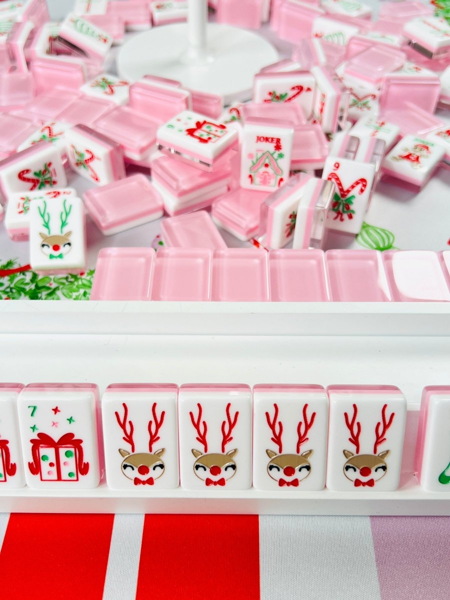 Holiday-themed mahjong tiles with pink backs and Christmas designs, including repeated reindeer tiles and a joker tile in a rack.
