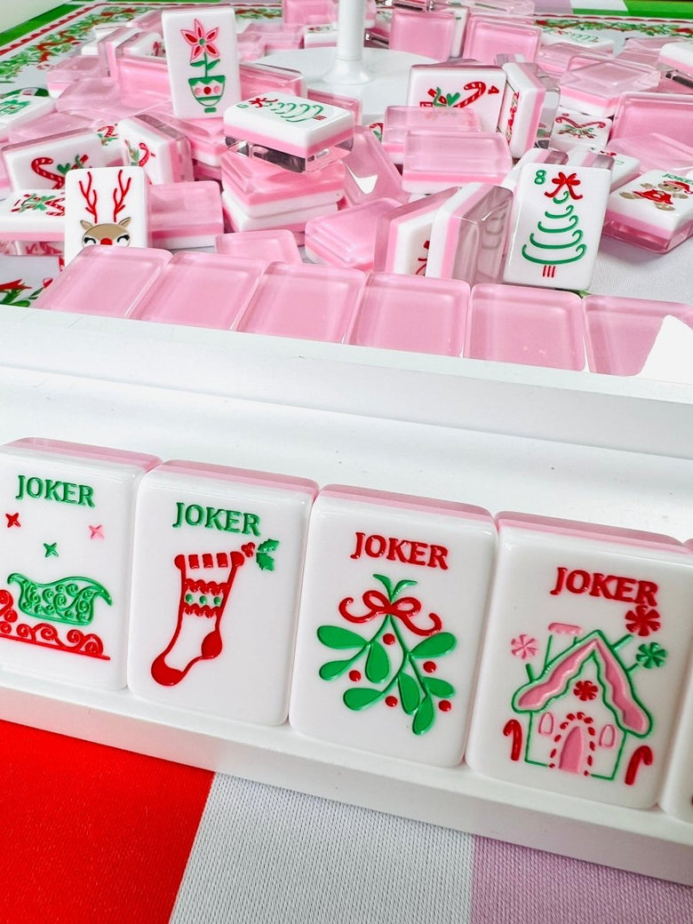 Holiday-themed mahjong tiles with pink backs and Christmas designs, including reindeer and four joker tiles displayed in a rack.